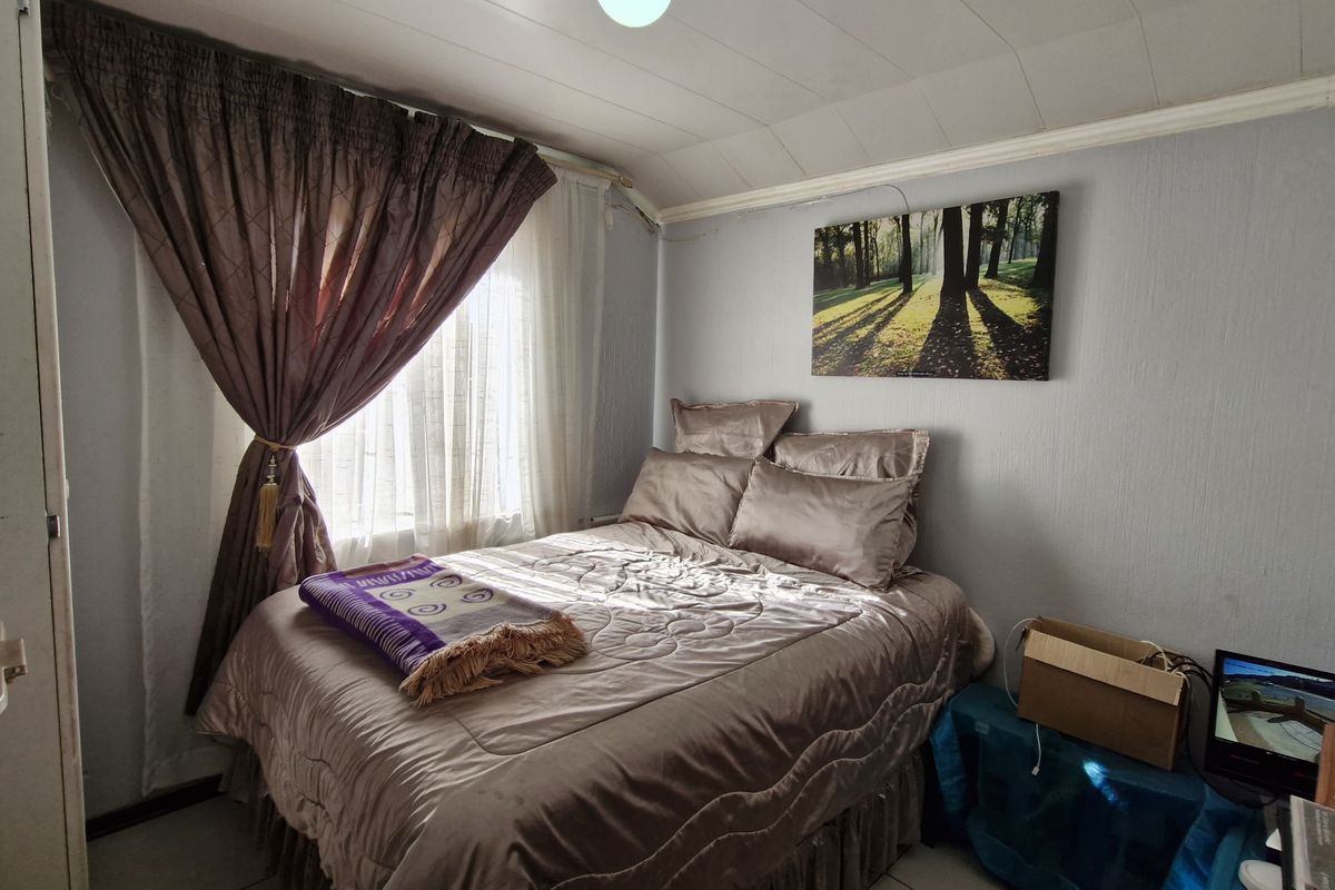 A compact bedroom featuring a tiled ceiling and a window with curtains, providing a functional sleeping space.