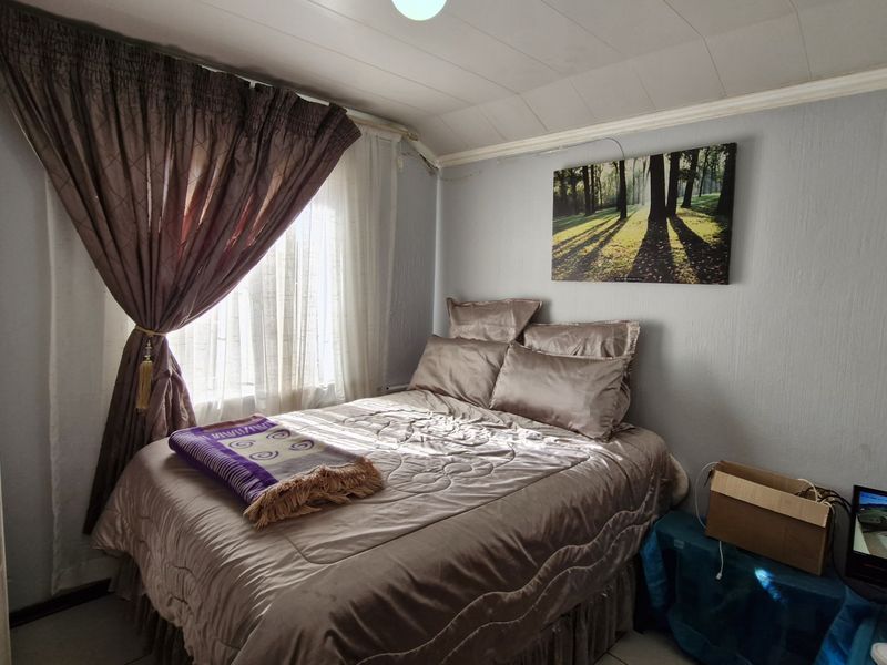 A compact bedroom featuring a tiled ceiling and a window with curtains, providing a functional sleeping space.