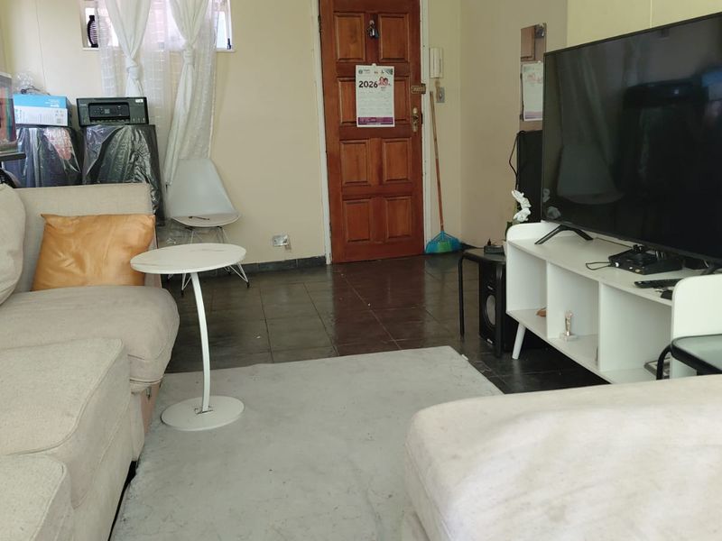 A living room area featuring tiled flooring and a timber entrance door, providing a functional space for relaxation.