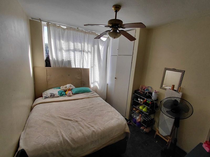A compact bedroom featuring a ceiling fan and a built-in wardrobe, providing essential storage and climate control.
