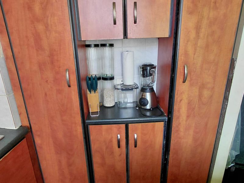 A kitchen storage unit featuring wood-look laminate cabinetry, dark countertops, and a tiled backsplash, providing functional pantry or appliance storage space.