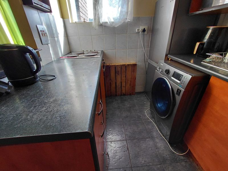 Compact kitchen featuring dark laminate countertops, a built-in electric hob, tiled backsplash, and tiled flooring with integrated cabinetry.