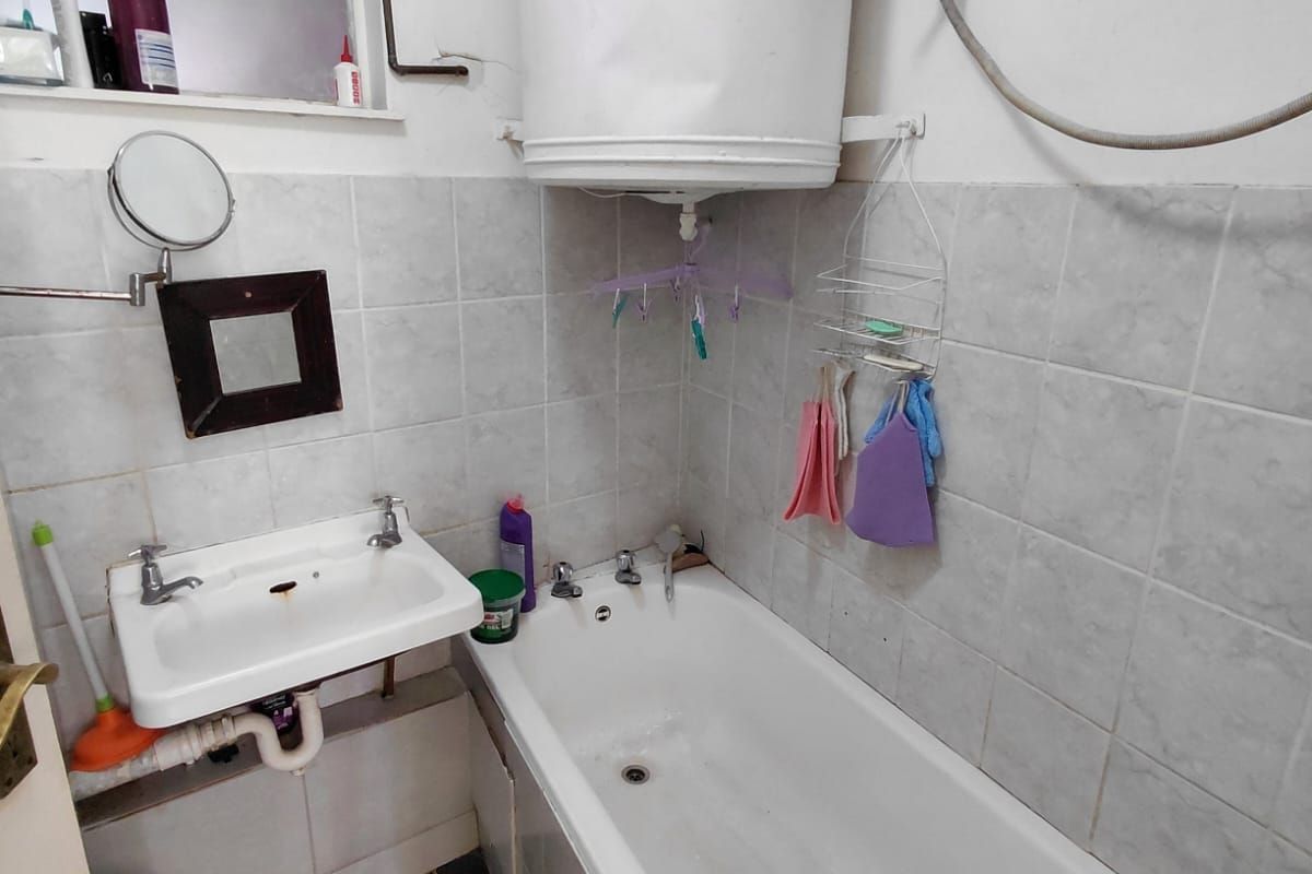 Compact bathroom featuring a wall-mounted geyser, standard bathtub, and wall-mounted basin with tiled splashbacks.