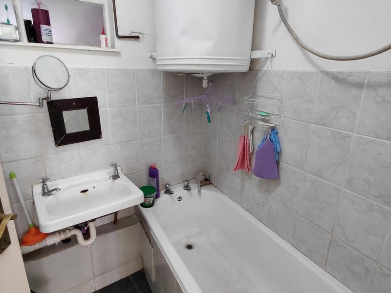 Compact bathroom featuring a wall-mounted geyser, standard bathtub, and wall-mounted basin with tiled splashbacks.