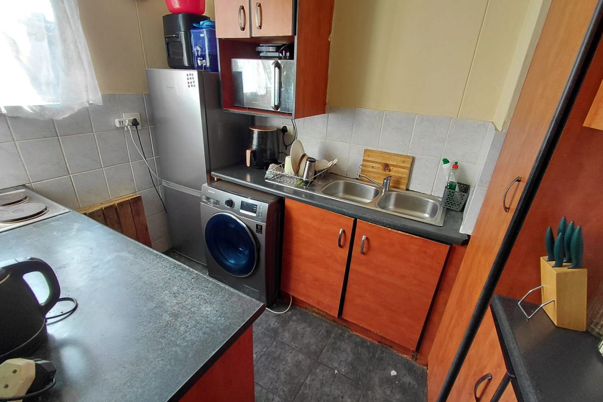 Compact kitchen featuring laminate cabinetry, double bowl stainless steel sink, tiled backsplash, and integrated hob, offering a functional layout for an apartment.
