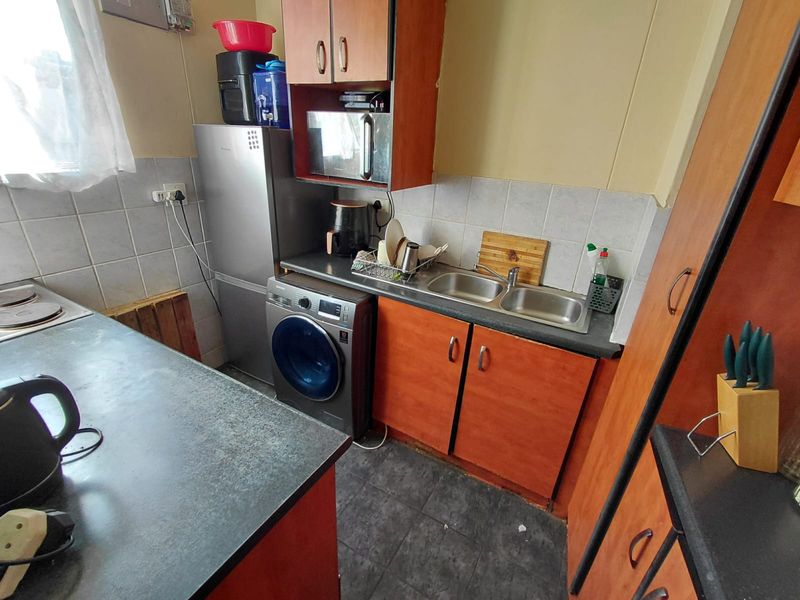 Compact kitchen featuring laminate cabinetry, double bowl stainless steel sink, tiled backsplash, and integrated hob, offering a functional layout for an apartment.
