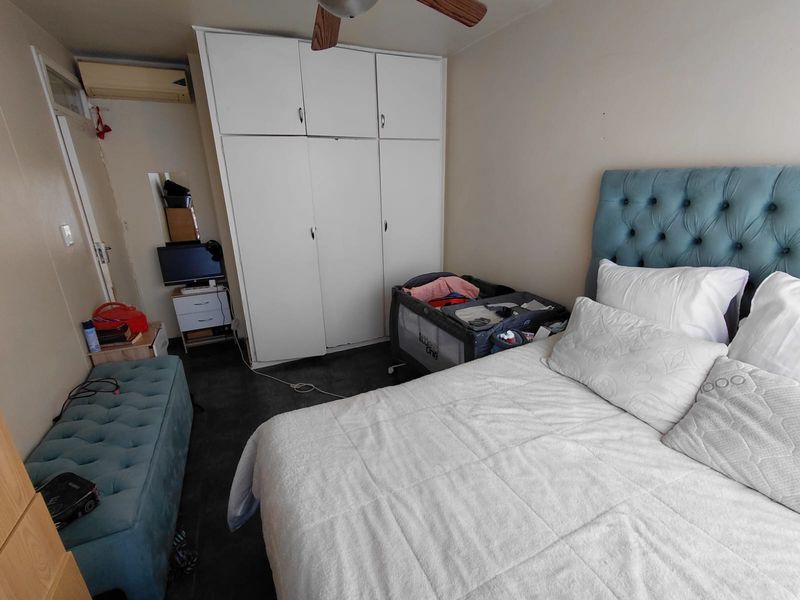 A functional bedroom featuring a built-in wardrobe, ceiling fan, and wall-mounted air conditioning unit, providing essential climate control and storage space.