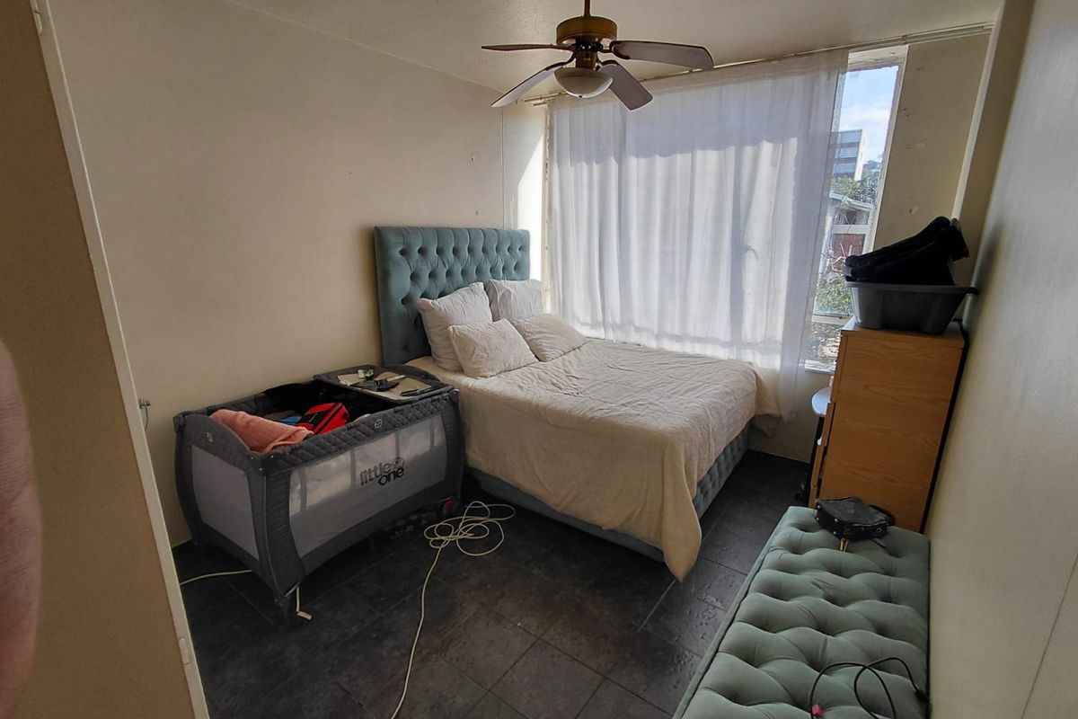 A bedroom featuring dark tiled flooring and a ceiling fan, with large windows allowing natural light into the space.