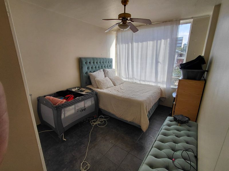 A bedroom featuring dark tiled flooring and a ceiling fan, with large windows allowing natural light into the space.