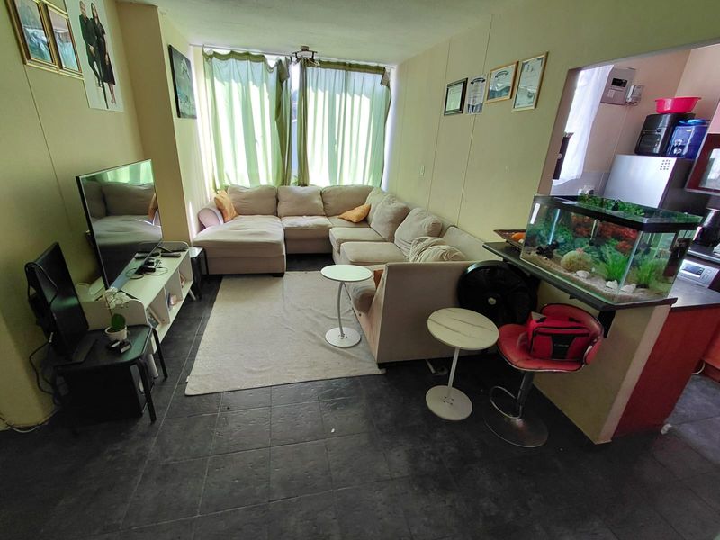 Open plan living area featuring dark tiled flooring and a pass-through window connecting to the kitchen space.