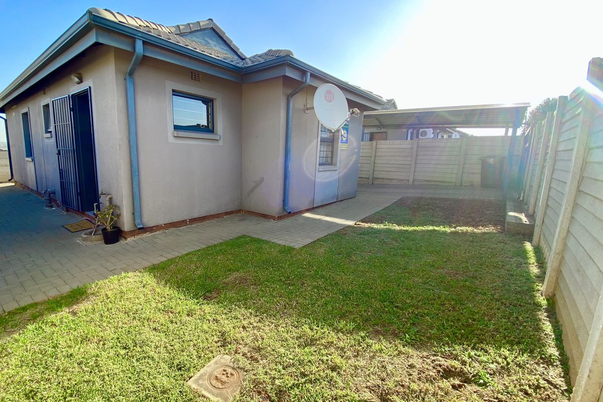 Rear exterior view of the property featuring a small lawn, paved patio area, and a carport structure enclosed by precast concrete boundary walls.