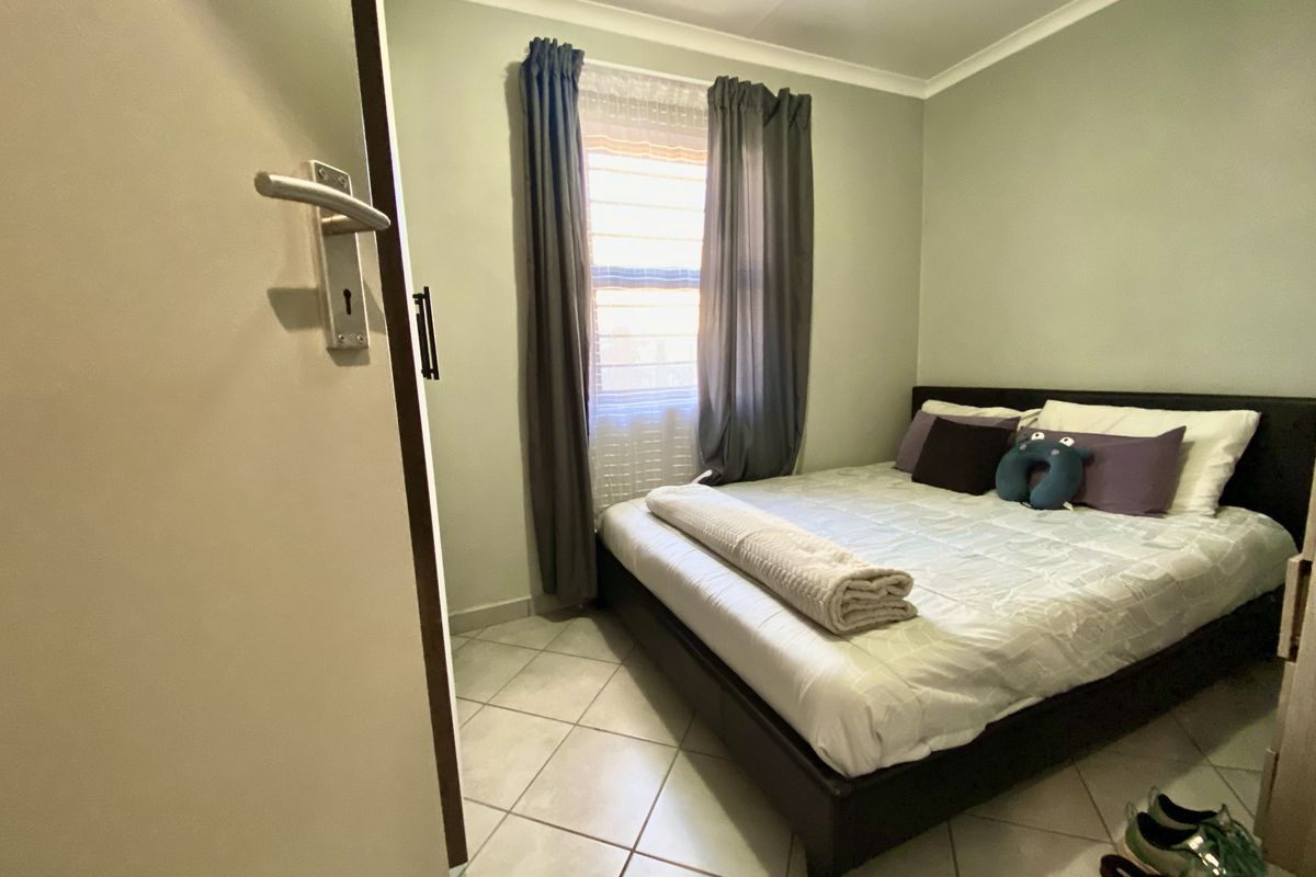 A compact bedroom featuring tiled flooring, neutral wall paint, and a window with curtain fixtures.