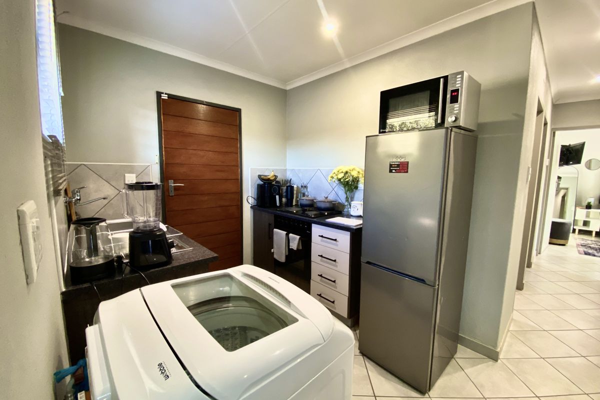 Compact kitchen featuring built-in cabinetry, tiled backsplash, and integrated cooking appliances, with adjacent laundry space and tiled flooring throughout.