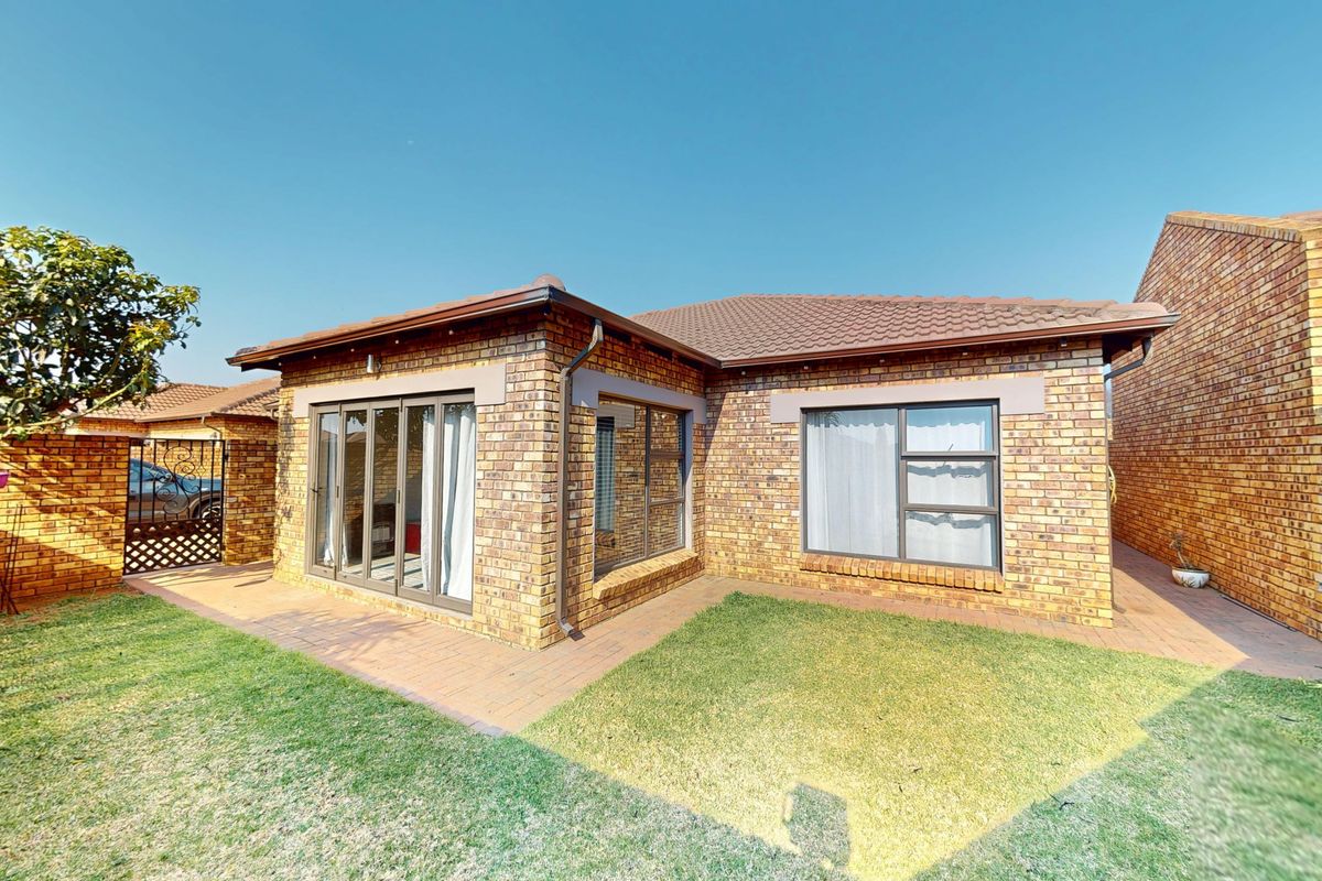 Rear view of a face brick cluster home featuring a paved patio, well-maintained lawn, and modern aluminium sliding doors and window frames.