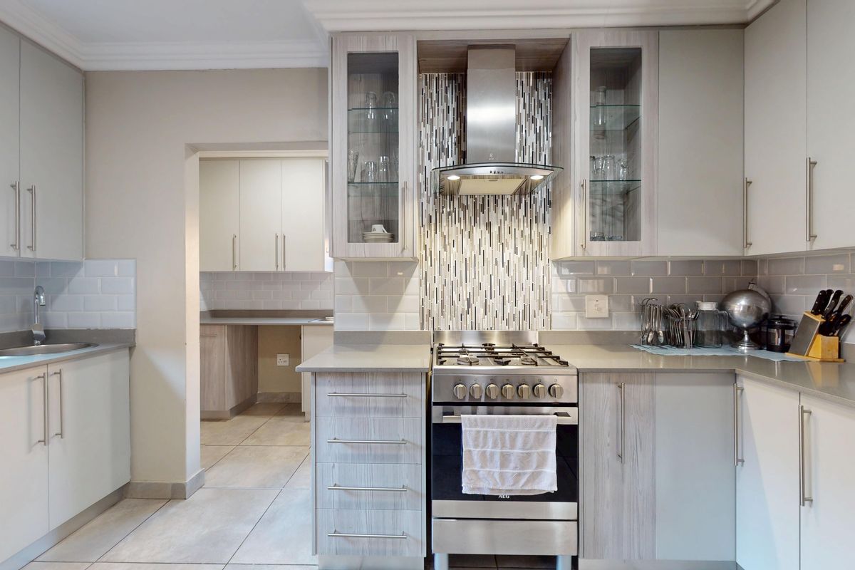 Modern kitchen featuring light wood-grain cabinetry, stone countertops, a gas stove with extractor fan, and a subway tile backsplash, with an adjoining scullery area.