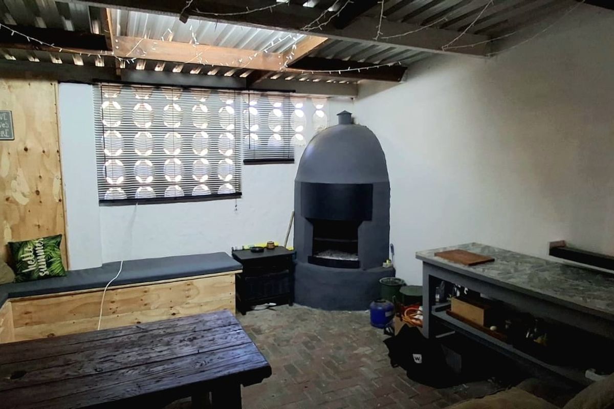 Covered outdoor patio area featuring a built-in fireplace, brick flooring, and built-in bench seating, offering a rustic space for outdoor entertaining.