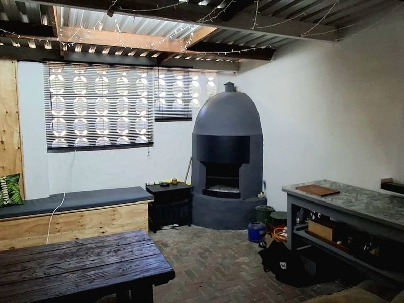 Covered outdoor patio area featuring a built-in fireplace, brick flooring, and built-in bench seating, offering a rustic space for outdoor entertaining.