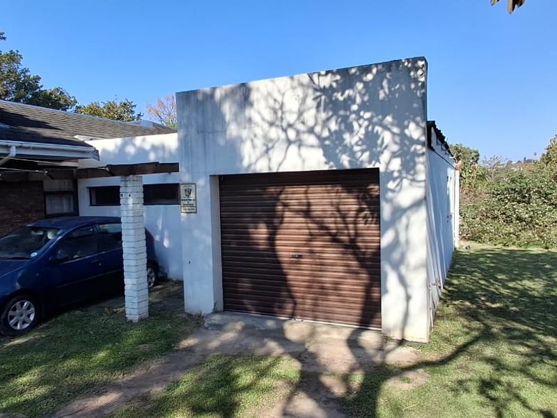 Front exterior view of the house featuring a single garage with a roller shutter door, a covered carport area, and a brick chimney.