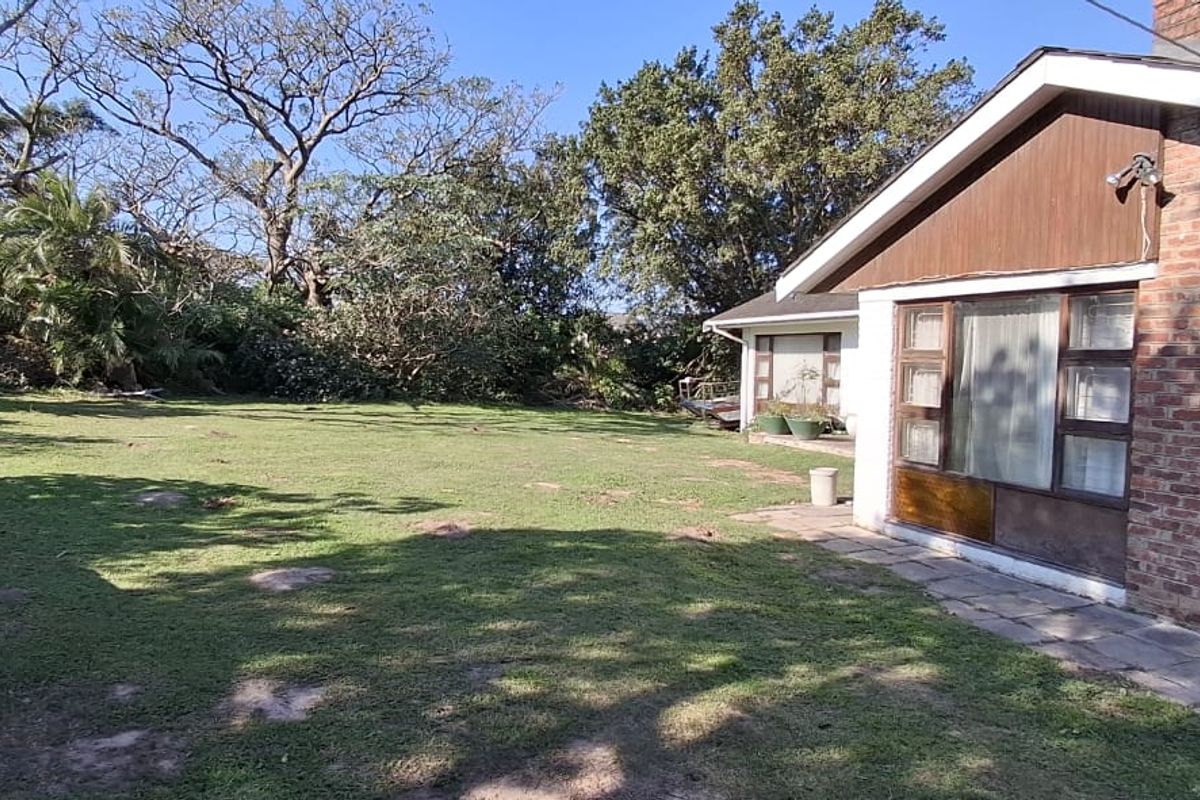 A view of the rear garden and the side of the brick house featuring a paved walkway and mature trees.