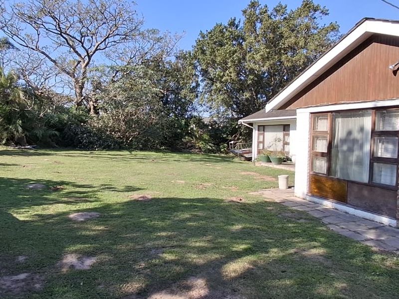 A view of the rear garden and the side of the brick house featuring a paved walkway and mature trees.