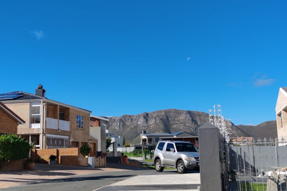 A street-level view of a residential neighborhood featuring paved driveways, brick homes with solar panels, and scenic mountain views in the background.
