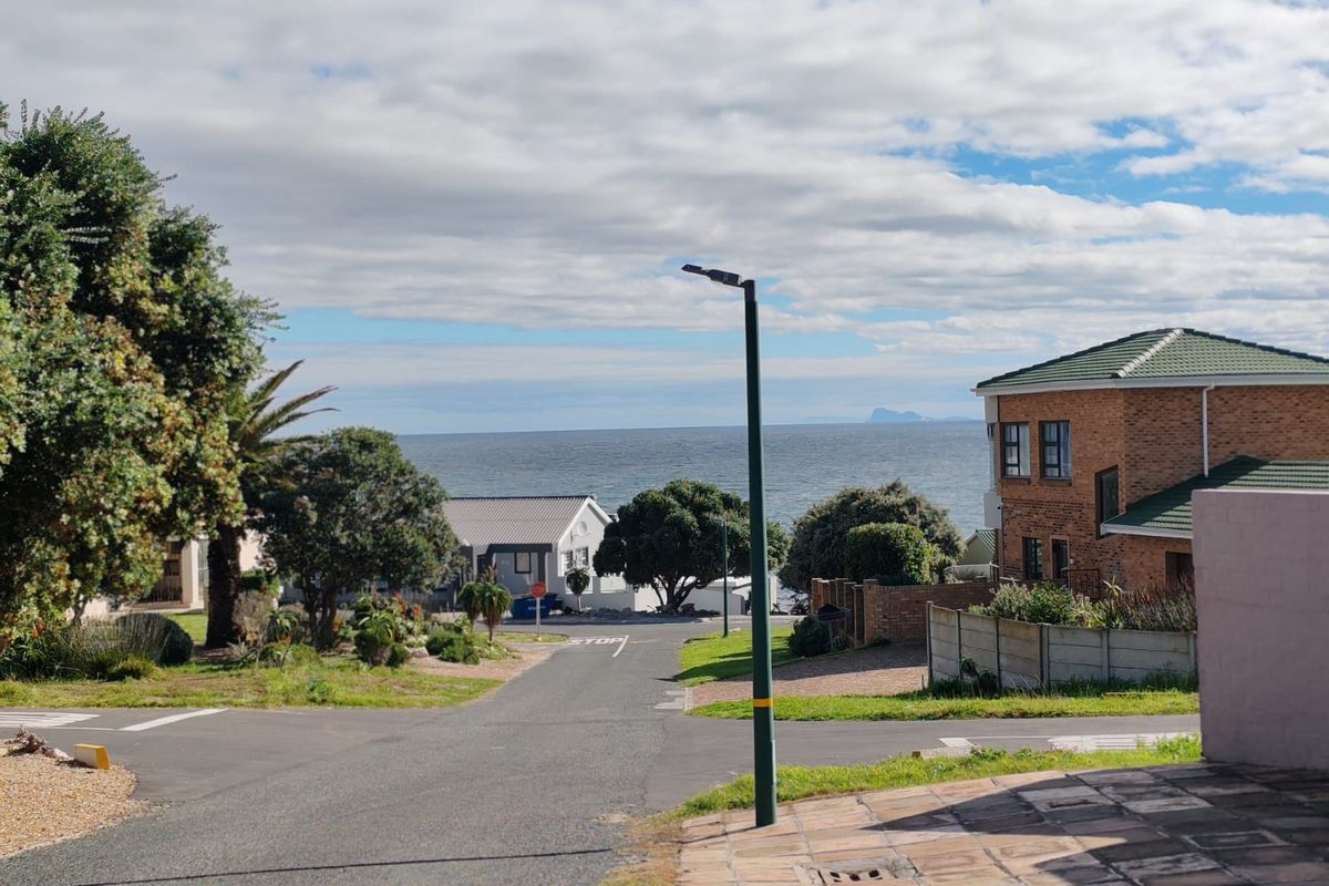 A street view looking down a residential road towards the ocean, showcasing the neighborhood approach and coastal surroundings.
