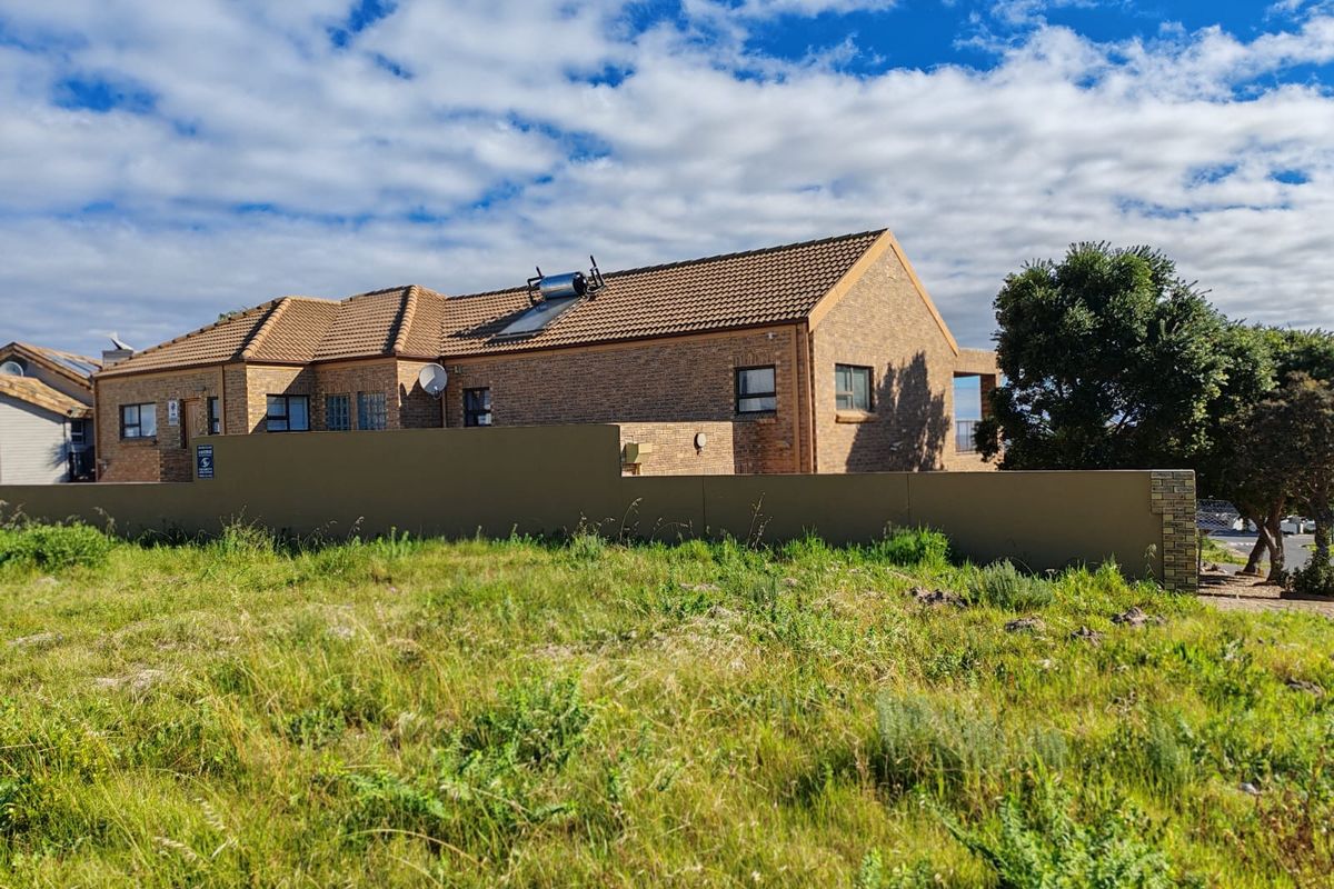 A view of the rear brick facade of a residential property featuring a tiled roof, solar water heating system, and a solid boundary wall.
