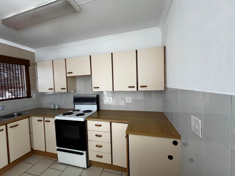 A dated kitchen featuring laminate countertops, built-in cabinetry, a freestanding stove, and ceramic tile flooring, offering potential for a modern renovation.