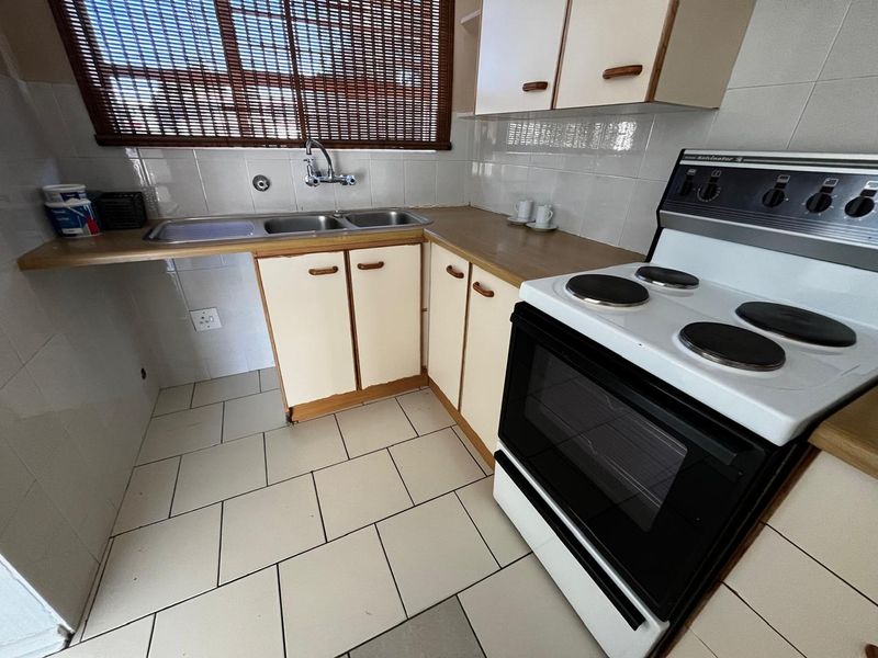 A functional kitchen featuring dated cabinetry, laminate countertops, a double sink, and a freestanding electric stove with tiled splashbacks and flooring.