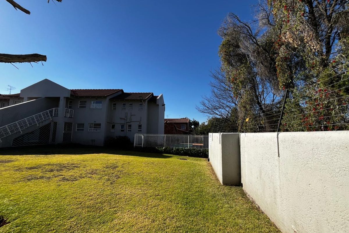 A view of the rear exterior of the apartment complex, featuring a well-maintained lawn, perimeter wall with electric fencing, and building facade.