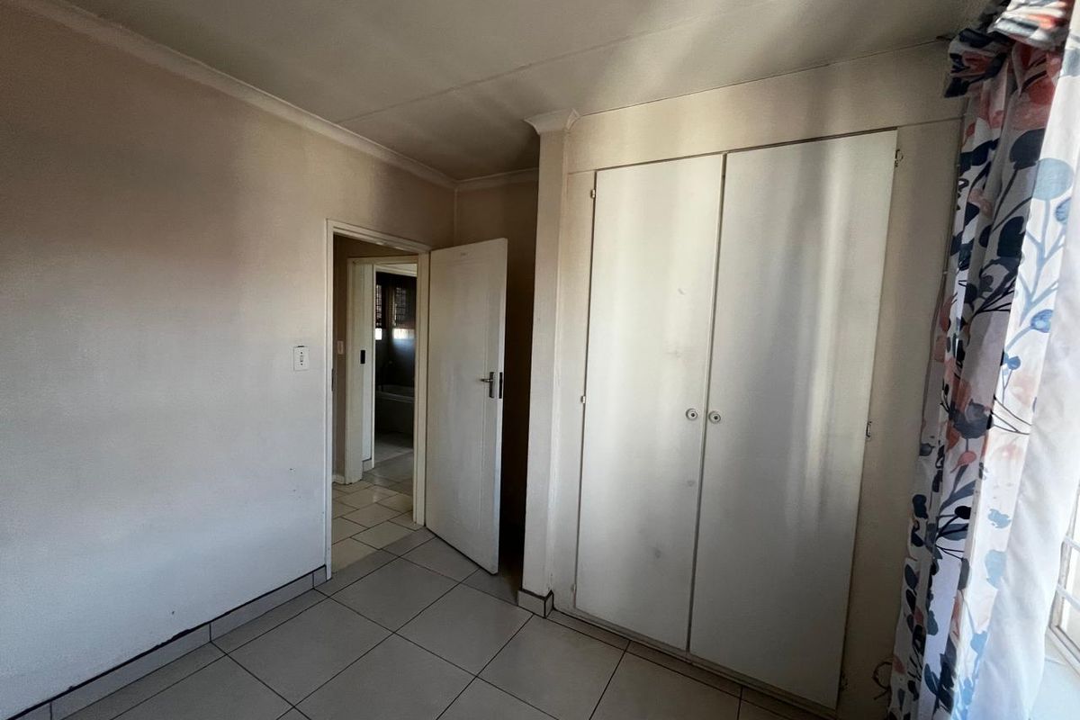 A vacant bedroom featuring tiled flooring, a built-in wardrobe, and coved ceilings, offering a blank canvas for renovation or staging.