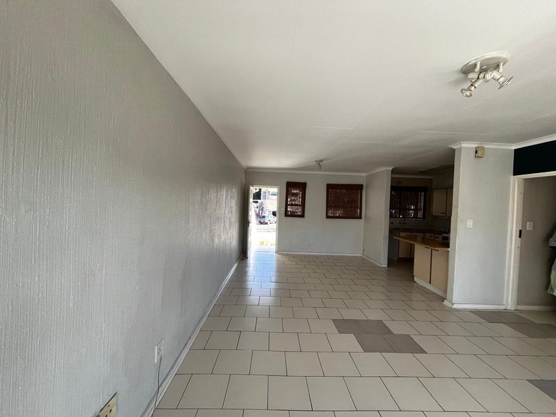 An open-plan living and kitchen area featuring tiled flooring, built-in cabinetry, and a breakfast counter, offering a blank canvas for renovation.
