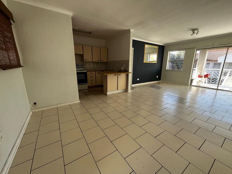 Open-plan living and kitchen area featuring tiled flooring, dated cabinetry, and sliding glass doors leading to an outdoor balcony space.
