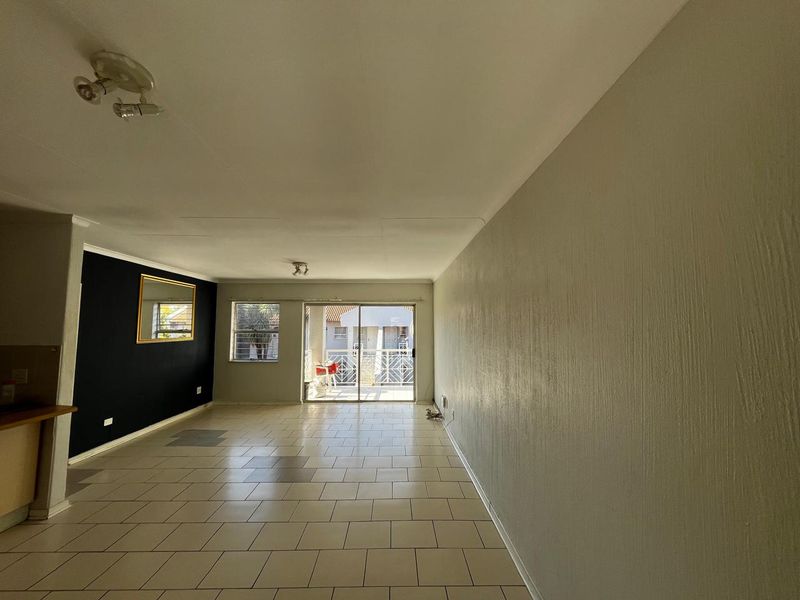 Spacious open-plan living area featuring tiled flooring, a sliding door leading to a balcony, and a neutral color palette with a feature wall.