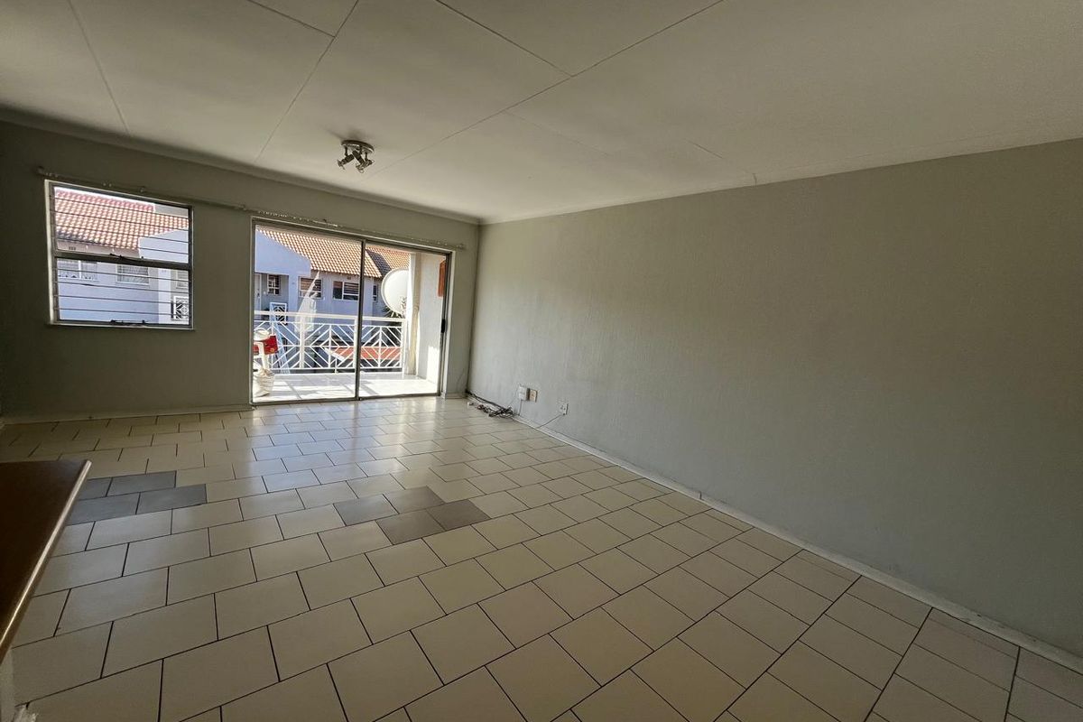 An empty, open-plan living area featuring tiled flooring and a sliding glass door providing access to an outdoor balcony.