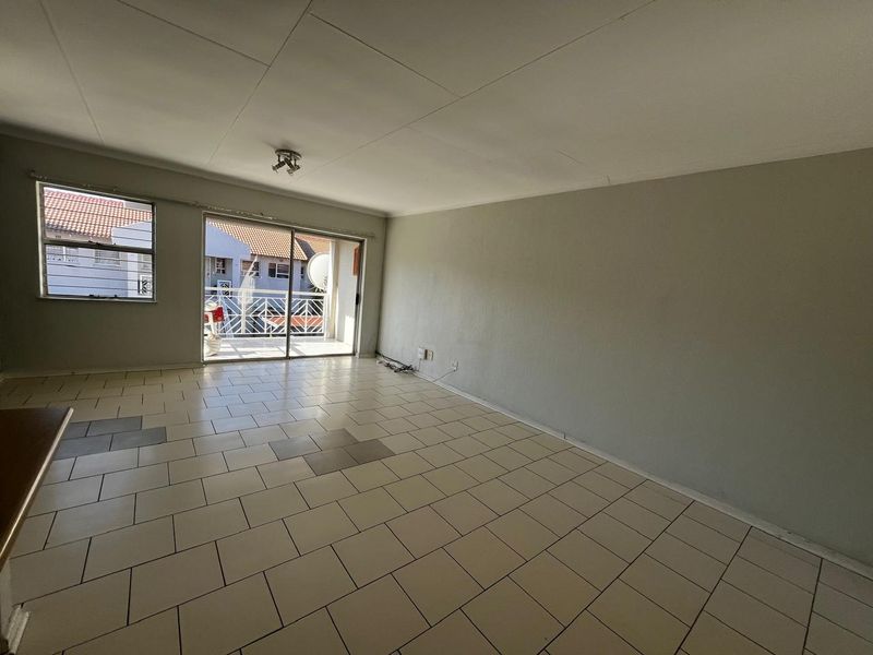 An empty, open-plan living area featuring tiled flooring and a sliding glass door providing access to an outdoor balcony.