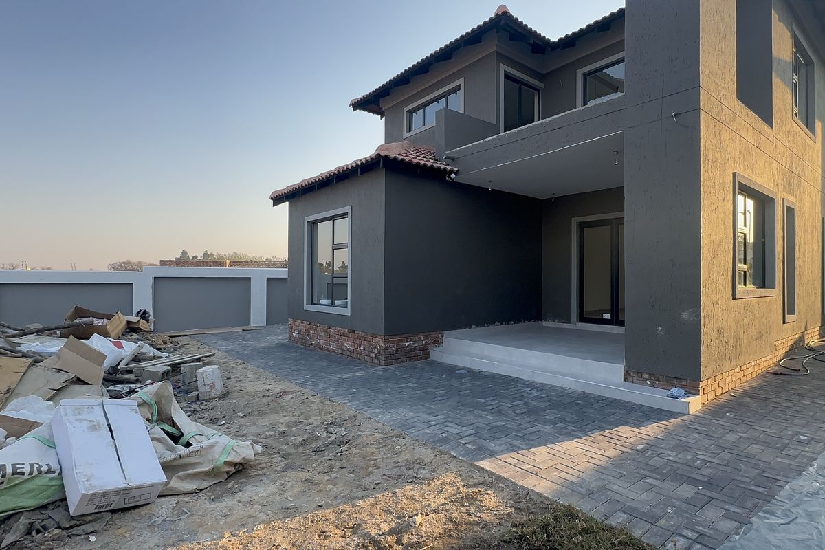Rear view of a modern double-storey house featuring a paved patio area, brick detailing, and a surrounding boundary wall, currently undergoing final exterior site works.