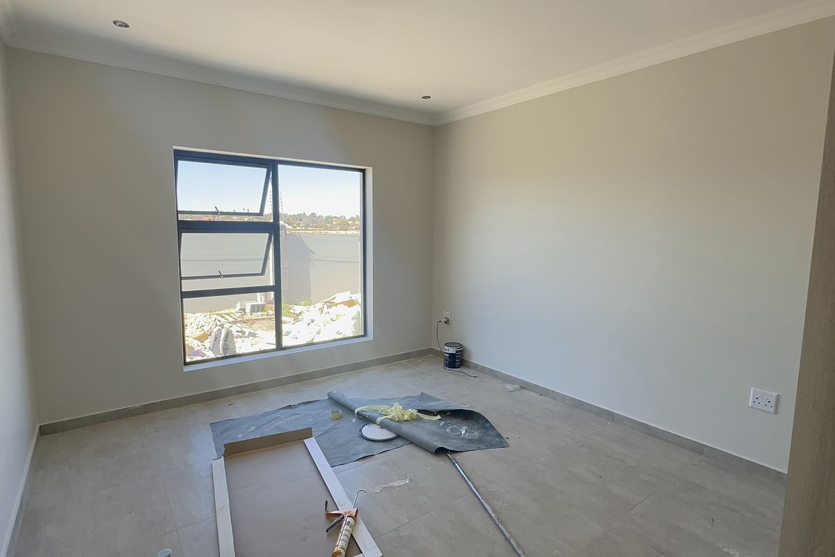 A bright, empty bedroom featuring modern tiled flooring, neutral walls, and a large aluminium-framed window, presenting a clean canvas for interior design.