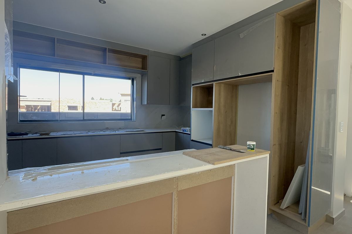A modern kitchen under construction featuring grey cabinetry, wood-look shelving, and a breakfast bar, currently awaiting final finishes and installation completion.