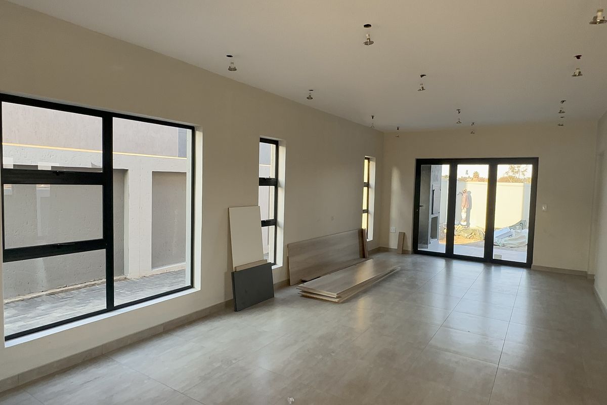 Spacious, light-filled living area featuring large aluminium windows, sliding doors to the exterior, and neutral tiled flooring, currently in a final construction phase.