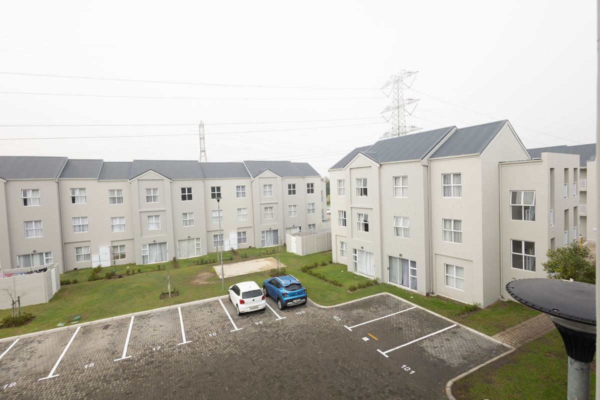 An elevated view of an apartment complex featuring a paved parking area, communal garden spaces, and multi-story residential buildings with metal roofing.