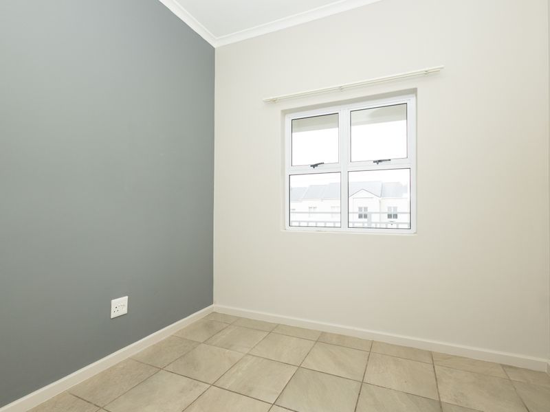 A clean, empty bedroom featuring neutral tiled flooring, a grey accent wall, and a window with a fitted curtain rail.