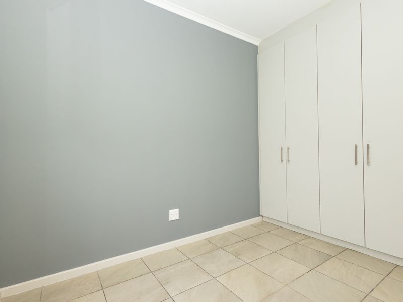 A clean, empty bedroom featuring neutral grey walls, tiled flooring, and ample built-in cupboard storage space.
