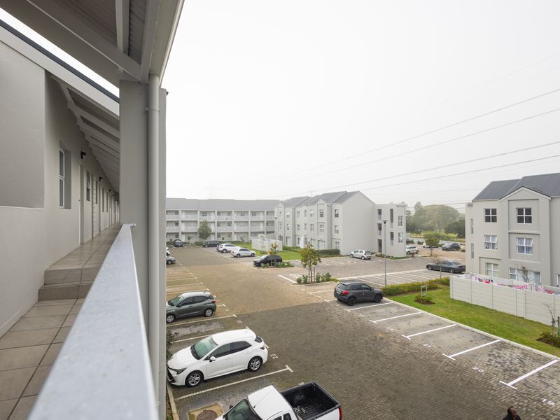 An elevated view from a covered apartment balcony overlooking the complex parking area and surrounding residential buildings.