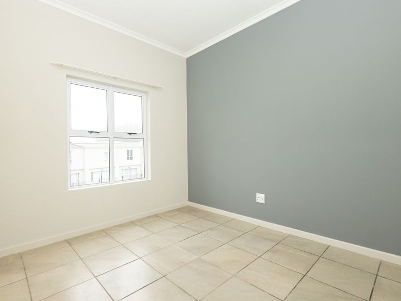 A bright, empty bedroom featuring neutral tiled flooring, a modern grey accent wall, and a large window providing natural light.