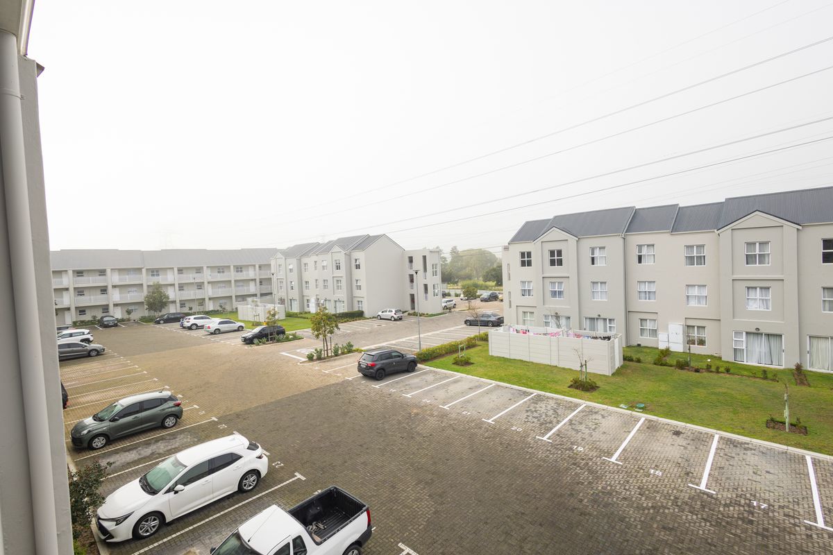 An elevated view of the apartment complex grounds, featuring paved parking bays, landscaped lawn areas, and multi-story residential buildings.
