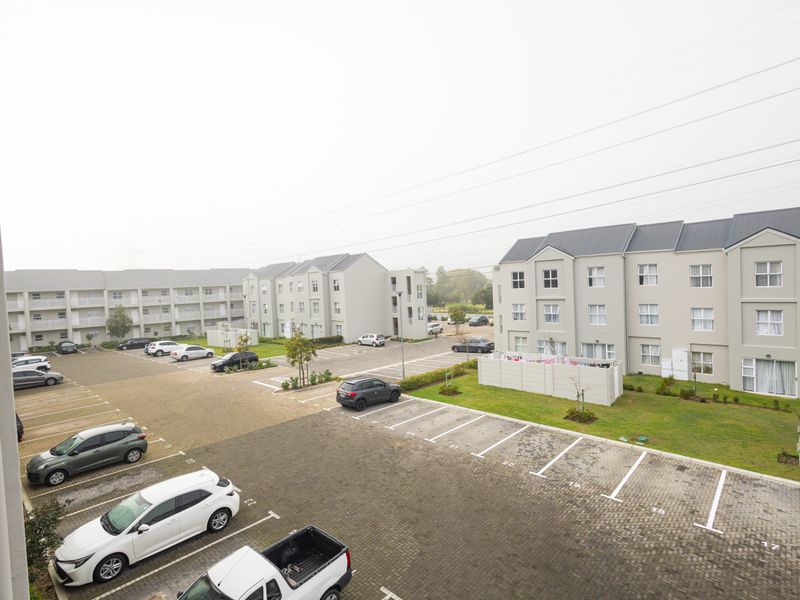 An elevated view of the apartment complex grounds, featuring paved parking bays, landscaped lawn areas, and multi-story residential buildings.
