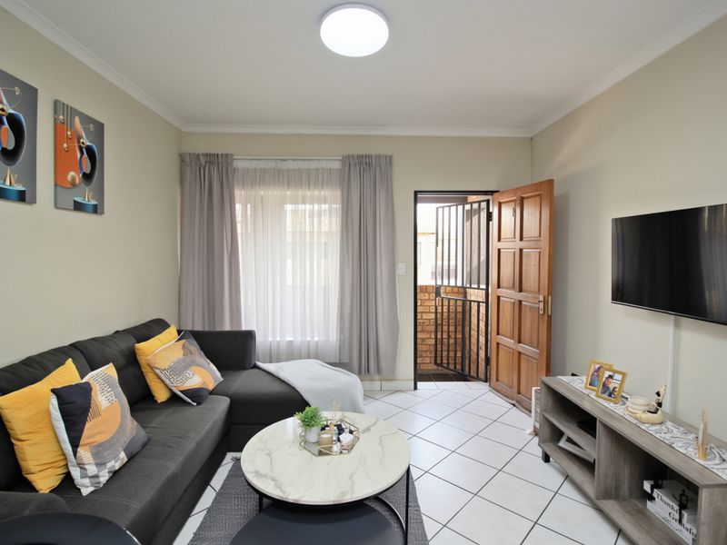 A well-maintained living room featuring tiled flooring, a timber entrance door with a security gate, and neutral wall finishes.