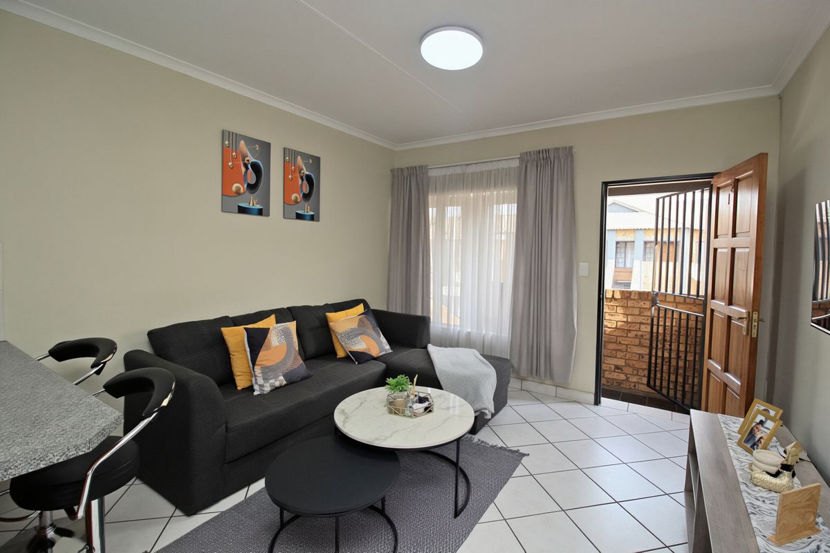 A well-maintained living room featuring tiled flooring, a ceiling light fixture, and direct access to an outdoor balcony through a secure entrance door.