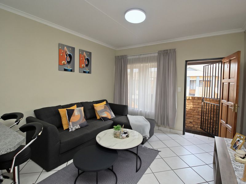 A well-maintained living room featuring tiled flooring, a ceiling light fixture, and direct access to an outdoor balcony through a secure entrance door.